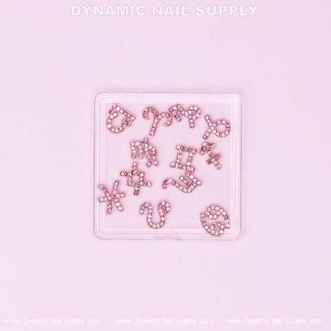 A clear container from Dynamic Nail Supply houses the Luxury Light Pink Zodiac Symbol Sign Nails Charm Set with Rhinestone, featuring intricately decorated charms for each zodiac sign. These light pink charms are embellished with sparkling rhinestones and arranged in a grid against a subtle light pink background with the brand name subtly displayed at the top.