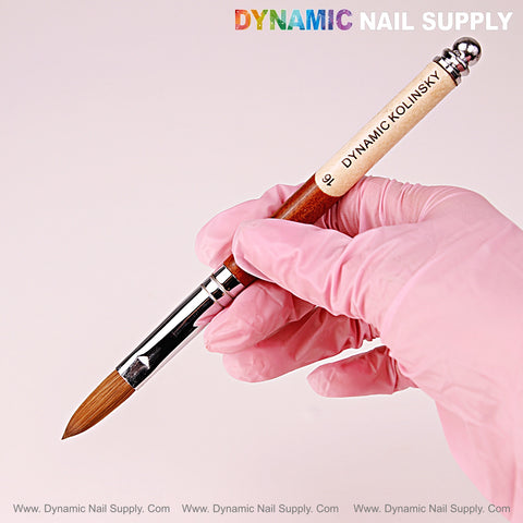 A hand in a pink glove holds the Crimped Size 16 Dynamic Kolinsky Brush against a light pink background.