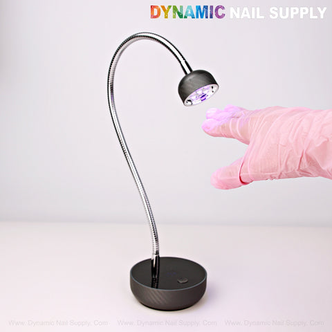 A pink-gloved hand reaches for the Long Goose Neck Flash Cure Lamp; DYNAMIC NAIL SUPPLY tops a white surface.