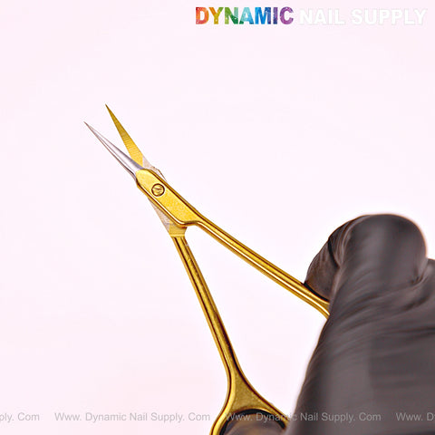 A gloved hand holds NT1245 Gold Premium Curved Tip Cuticle Scissors; Dynamic Nail Supply logo at top.