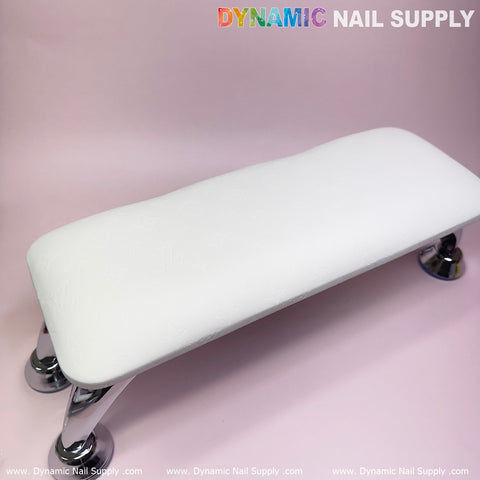 A white full-grain leather armrest cushion with an LV pattern on chrome legs rests on a light pink surface, ideal for manicure services. This armrest showcases subtle designer-inspired embossed patterns. In the top right corner, "Dynamic Nail Supply" appears in colorful and gray text, with repeated branding below.