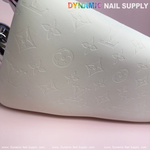 The product image showcases a close-up of the full-grain leather armrest cushion pillow for pedicure manicure, featuring an intricate embossed pattern of flowers and intertwined letters V and L on a smooth white surface. The texture is highlighted with subtle shadows and topped by the colorful and gray text "Dynamic Nail Supply," making it an ideal addition to elevate any manicure service ambiance.