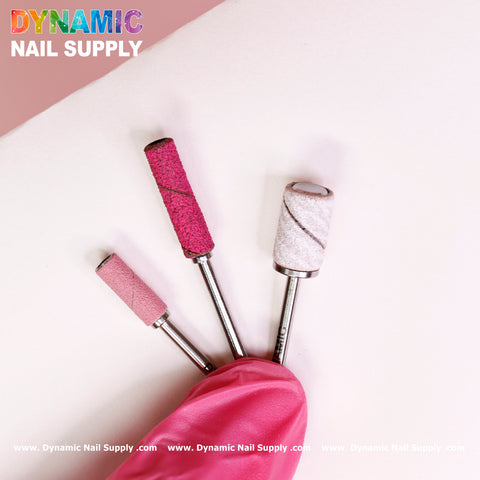 Three nail drill bits featuring textured pink and white cylindrical tips are elegantly displayed against a white background. A pink sleeve partially covers the base, making it ideal for use with the Dynamic Nail Supply Small 3.5mm Easy-Off Mandrel for Smaller Sanding Band. The Dynamic Nail Supply logo is prominently positioned in the top left corner, while their website URLs are repeated along the bottom edge.