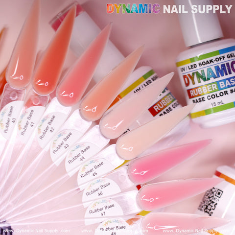A display showcases a range of stiletto-shaped nail samples in different hues of pink and nude, labeled as the (BIAB) Rubber Base Gel (Builder Gel in a Bottle) Number 40 to 48 collection. A bottle from Dynamic Nail Supply is partially shown, with the website address dynamicnailsupply.com at the bottom.