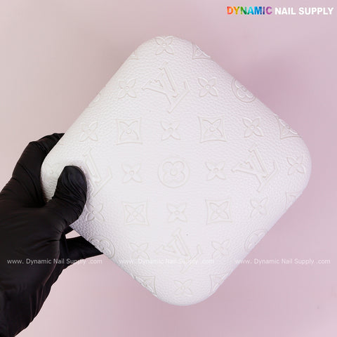 A gloved hand holds the White LV Engrave - Grain PU Leather Elbow Rest Pad for Nail Tech on a light pink background.