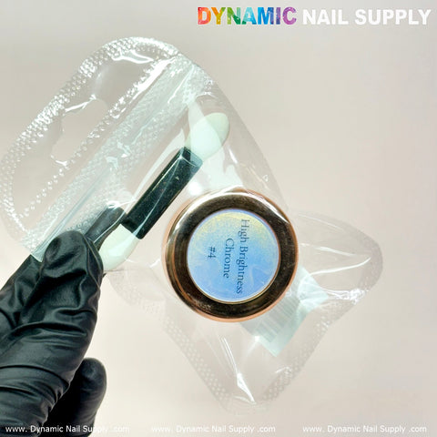 A gloved hand holds a small transparent package from Dynamic Nail Supply, showcasing a jar labeled Light-Mermaid Iridescent Chrome #10, renowned for its high brightness fine pigment powder that creates stunning iridescent chrome effects in nail art design. The package also includes a dual-ended makeup applicator, against a plain and light background.