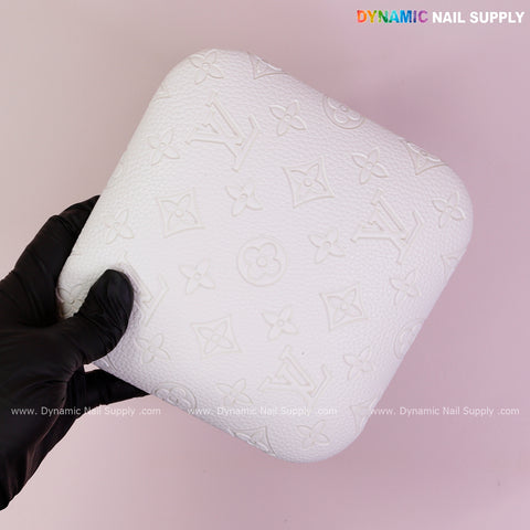 A gloved hand holds the White LV Engrave-Grain Elbow Rest Pad for Nail Techs on pink, with Dynamic Nail Supply text.