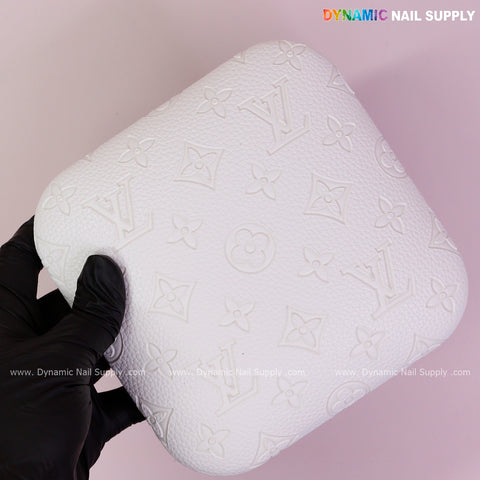 A gloved hand holds the White LV Engrave Elbow Rest Pad for Nail Tech, PU leather, on a pink background.