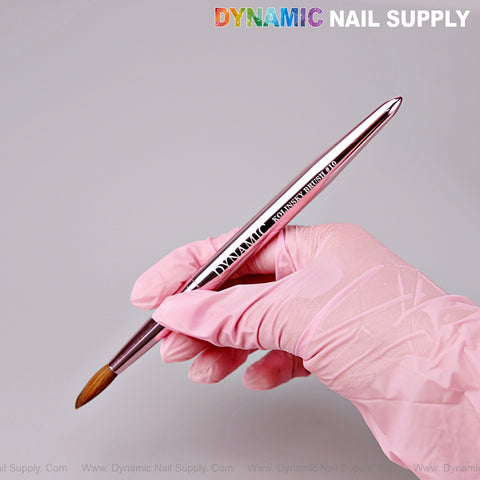 A gloved hand holds the Dynamic Metallic Pink 100% Pure Kolinsky Hair Brush for nails; DYNAMIC NAIL SUPPLY above.