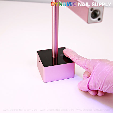 A nail tech uses the 2 in 1 Mini UV/LED Flash Cure Handheld Light with Stand Lamp, pressing its black top on a white surface.