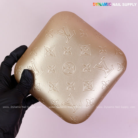 A hand holds a Metallic Gold LV Engrave Elbow Rest Pillow for Nail Tech on a light purple background.