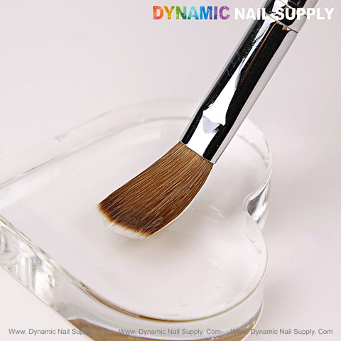 A Size 16 Dynamic Kolinsky Brush with brown bristles rests on a clear, heart-shaped dish; logo is at the top.