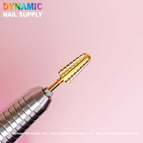 Close-up of a premium 2XC Volcano Bit by Dynamic Nail Supply, crafted from durable tungsten carbide with a textured cylindrical design, attached to a metallic handle against a pink background. The brand's logo in rainbow colors is displayed at the top left corner, with the website URL across the bottom edge.