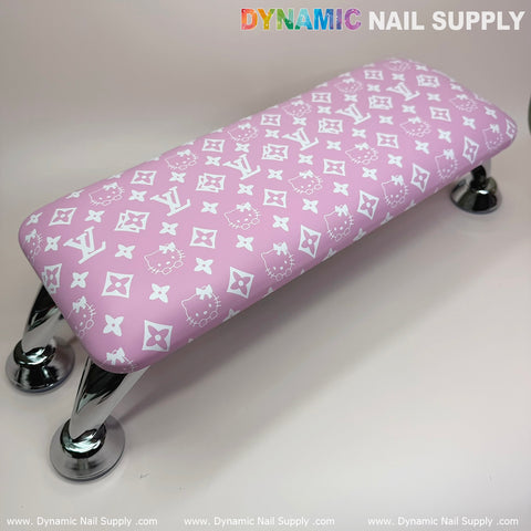 A pink leather armrest cushion featuring a designer-inspired pattern, supported by chrome legs, is ideal for manicure services. The Dynamic Nail Supply logo appears at the top and bottom of the image for the Pink Hell0 Kitty LV Nails Pillow ArmRest with Leather Cushion for Manicure Pedicure.