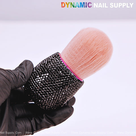 A gloved hand holds an RB10 Black Rhinestone Small Dust Brush by Dynamic Nail Supply at the top.