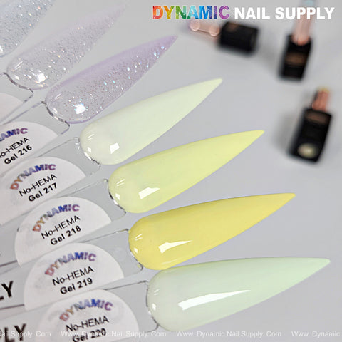 Five pastel nail swatches, glittery white to pale yellow, with Dynamic No-HEMA Gel Polish 211–220 bottles blurred behind.