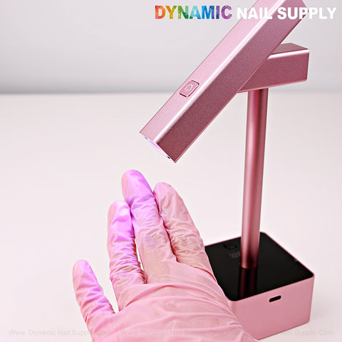 A gloved hand holds the 2 in 1 Mini UV/LED Flash Cure Light under purple glow and the Dynamic Nail Supply logo.