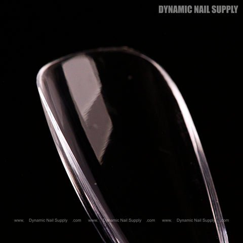 A clear, glossy Natural Stiletto (Medium) Full Cover Soft-Gel Nail Tip (Pink Box) on black with logo in corner.