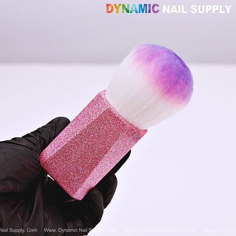 A gloved hand holds the Ombre Pink Glitter Small Dust Brush for Cleaning Up, with white and purple bristles; DYNAMIC NAIL SUPPLY is at the top.