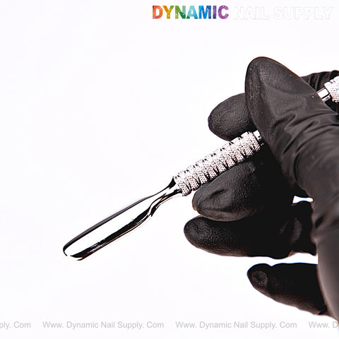 A gloved hand holds the NT1230 – Professional Double-Function Cuticle Pusher under the Dynamic Nail Supply logo.