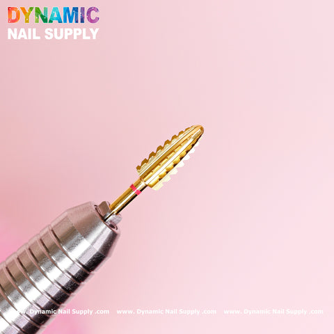 Close-up of a metallic nail drill featuring the 2XC Typhoon Bit, a double extra coarse gold conical bit specifically designed for removing acrylic or gel polish, set against a soft pink background. The silver drill is equipped with horizontal grooves for enhanced grip. In the upper left corner, the brand name Dynamic Nail Supply is prominently displayed in colorful bold letters.