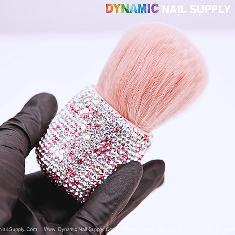 A gloved hand holds the AB-Pink Rhinestone Small Dust Brush, a cleaning tool for acrylic nails and powder removal.