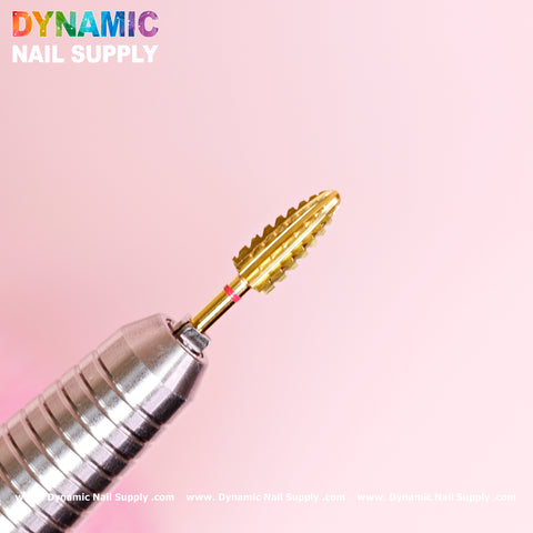A close-up of the 2XC Typhoon Bit from Dynamic Nail Supply shows off its silver drill bit and gold, cylindrical, grooved grinding head set against a soft pink background. Built for precise removal of gel polish or acrylic surfaces, the design is complemented by the Dynamic Nail Supply logo in multicolored text at the top left, with subtle website URLs repeating along the bottom.