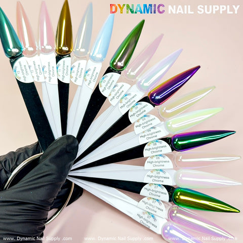 A hand in a black glove holds a ring displaying nail design swatches in teardrop shapes, including shades from iridescent chrome powder like Light-green/Purple/Mermaid Iridescent Chrome #08 to soft pastels. Set against a pink background, Dynamic Nail Supply is prominently featured at the top, with each swatch distinctly labeled by its unique color name.