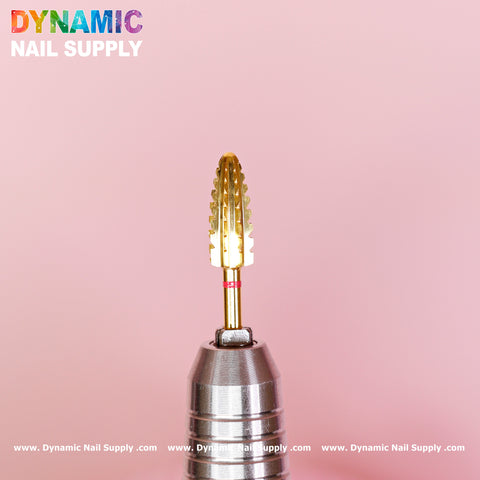 An image features the 2XC Typhoon Bit by Dynamic Nail Supply, a gold acrylic nail drill bit designed with a textured cylindrical shape attached to a metal drill handle. The background is light pink, and "Dynamic Nail Supply" appears in multicolored text at the top left and bottom of the image.