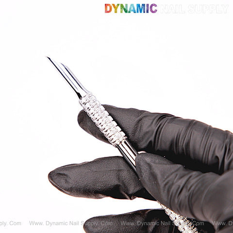 A gloved hand holds the NT1231 Professional Double-Function Cuticle Pusher; DYNAMIC NAIL SUPPLY logo is above.