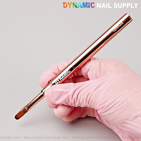 A gloved hand holds the Rose Gold Builder Poly Hard Gel Dual Head Nail Art Brush with oval brush and spatula ends.