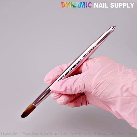 A pink-gloved hand holds the Dynamic Metallic Pink 100% Pure Kolinsky Hair Brush; logo appears in the top right corner.