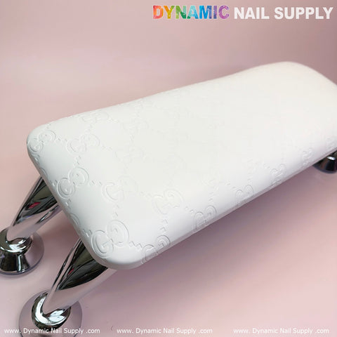 A Super White GC Leather Armrest with Cushion Pillow for Pedicure Manicure is displayed on a light pink surface, featuring metallic curved legs for support. The Dynamic Nail Supply branding is prominently shown at the top and bottom of the image, suggesting luxurious manicure services.
