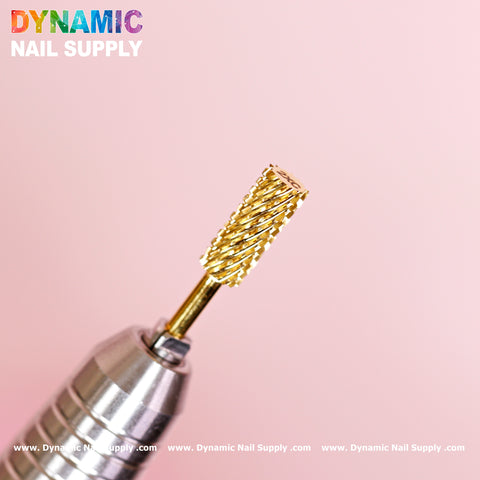 A close-up of a shiny, gold 2XC Double Extra Coarse Drill Bit - Small Barrel Carbide, featuring a textured cylindrical design, is set against a soft pink background. This drill bit, perfect for gel or acrylic nail removal, shows off its silver base. The logos and text reading "Dynamic Nail Supply" appear at the top and bottom edges.