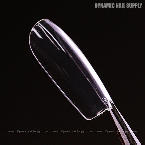 A Sculpted Square (Medium) Full Cover Soft-Gel Nail Tip (Black Box) is held by tweezers on a black background.