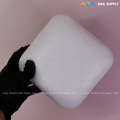 A black-gloved hand holds the White GC Engrave - Smooth Elbow Pad Pillow for Nail Tech against a pink background.
