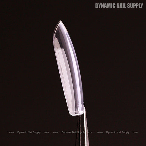 A Sculpted Square (Medium) Full Cover Soft-Gel Nail Tip from the Black Box held by tweezers against a black background.