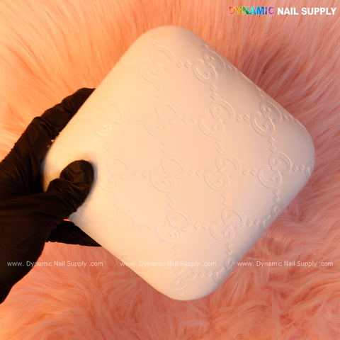 A gloved hand holds the White GC Engrave Elbow Pad Pillow—smooth PU leather, ideal for nail techs on pink fur.