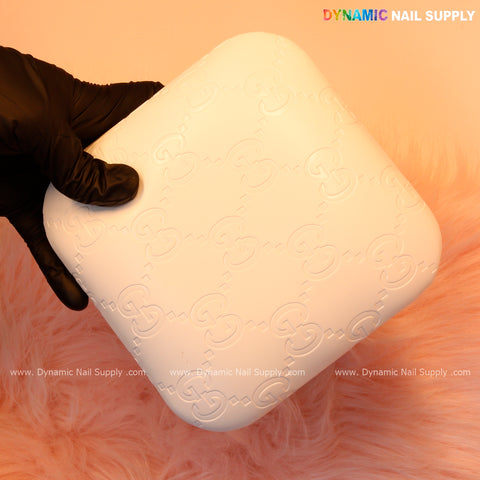 A gloved hand holds the White GC Engrave - Smooth Elbow Pad Pillow for Nail Tech on a pink fur surface.