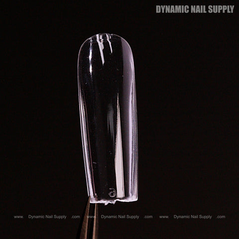 A Sculpted Square (Long) Full Cover Soft-Gel Nail Tip (Pink Box) held by tweezers against a black background.