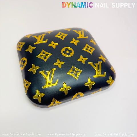 The Leather Elbow Cushion Pad Arm Rest Support for Manicure Nail Desk by Dynamic Nail Supply features a square black design made from PU leather. It displays a pattern of golden yellow symbols reminiscent of a luxury brand's monogram and floral motifs. Set on a plain white background, the words "Dynamic Nail Supply" appear along the top and bottom edges, adding a touch of elegance to any manicure nail desk.