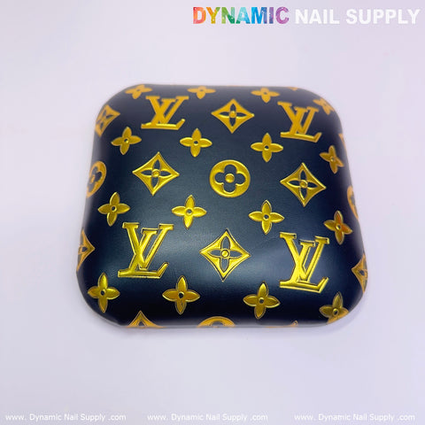 A square, navy blue arm rest cover crafted from PU leather material features a pattern of gold monogram symbols, reminiscent of luxury brand motifs. The design incorporates floral and geometric shapes. At the top, it reads "Dynamic Nail Supply" in colorful, bold letters against a plain white background.