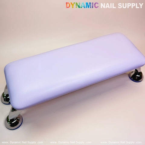 A microfiber leather armrest cushion in purple, designed with a rectangular shape and chrome legs, is set against a neutral background. In the top left corner, the text "Dynamic Nail Supply" is displayed in colorful and gray letters, making it an ideal addition to enhance any manicure service setting.