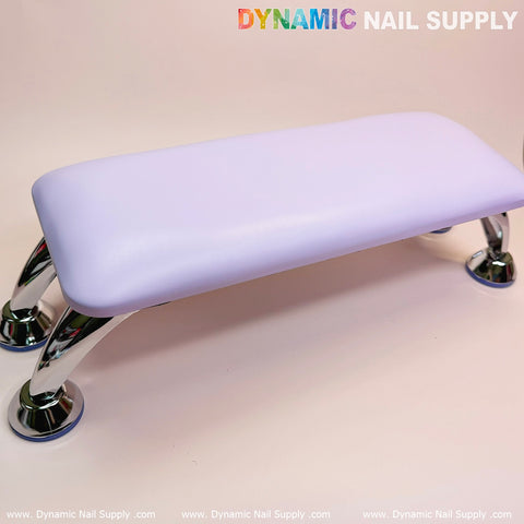 Displayed against a soft pink backdrop is the Purple Microfiber Leather Armrest with Cushion Pillow for Pedicure Manicure by Dynamic Nail Supply, featuring a sleek leather cushion and shiny metal legs. This comfort-focused design enhances the manicure service experience, with the text DYNAMIC NAIL SUPPLY visible at the top of the image.