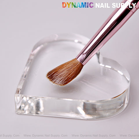 A Dynamic Metallic Pink Kolinsky Nail Brush rests on a clear heart glass palette, with DYNAMIC NAIL SUPPLY text above.