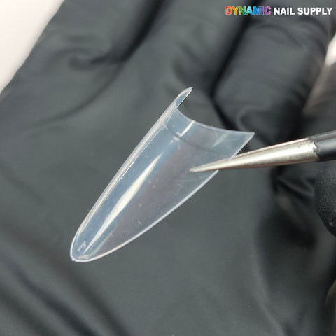 A gloved hand holds Medium Almond Extension Nail Tips; a metal tool points to the edge. “DYNAMIC NAIL SUPPLY” appears.