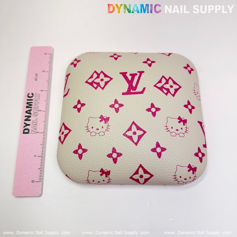 A leather elbow cushion pad, square in shape and beige with pink Hello Kitty and floral designs plus a prominent LV emblem, makes an ideal manicure nail desk accessory. The product, from Dynamic Nail Supply, is shown alongside a pink ruler bearing the same brand name on a white background.