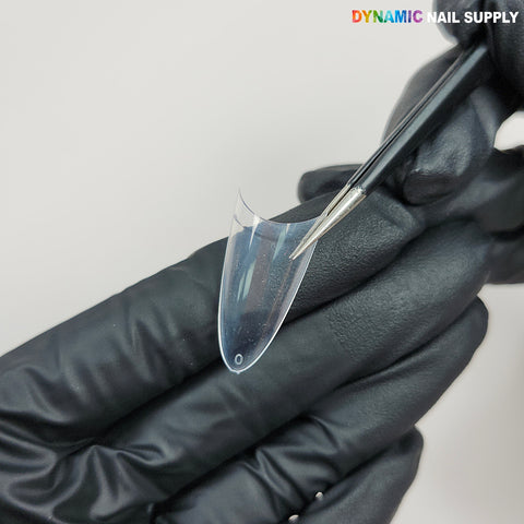 A gloved hand holds a (New 2026) Medium Almond Extension Nail Tip as a brush applies product, logo in the corner.