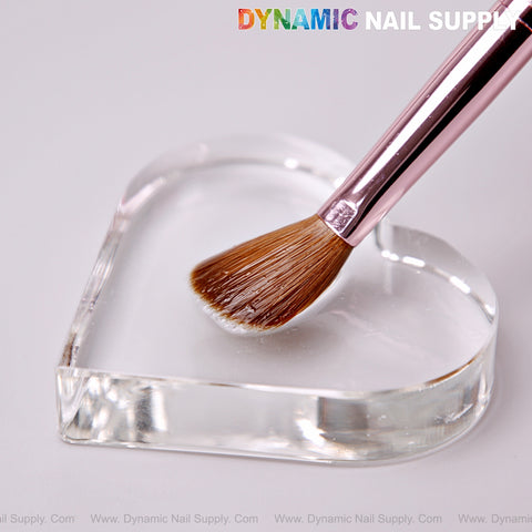 A Dynamic Metallic Pink Kolinsky Nail Brush rests on a clear heart-shaped dish with “DYNAMIC NAIL SUPPLY” at the top.