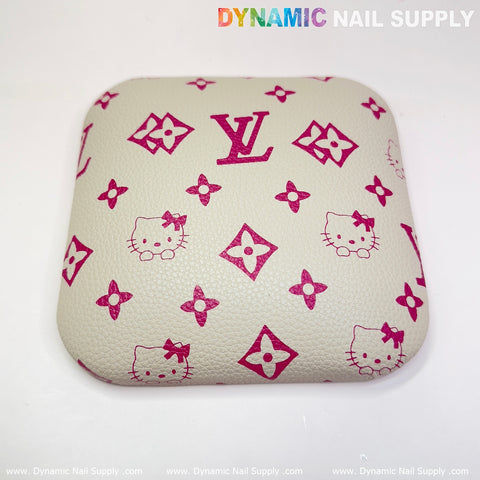 Introducing the Beige LV+Kitty Pattern Leather Elbow Cushion Pad Arm Rest Support for your manicure nail desk, designed by Dynamic Nail Supply. This square cushion showcases a cream-colored base with a textured surface, adorned with charming Hello Kitty faces and floral motifs in pink. The top features vibrant "Dynamic Nail Supply" text, with a subtle repeat at the bottom border, making it ideal for use as an elbow pad or arm rest support.